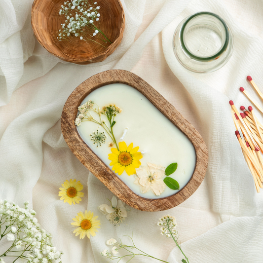 Candle in a wooden dish with flowers on a white fabric background