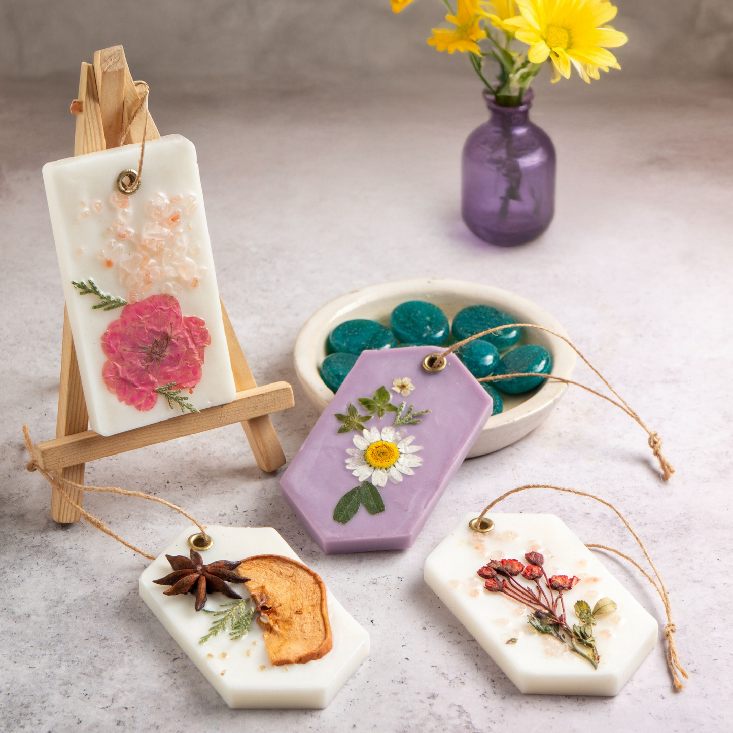 Decorative soaps with floral designs on a gray surface with a vase of yellow flowers.