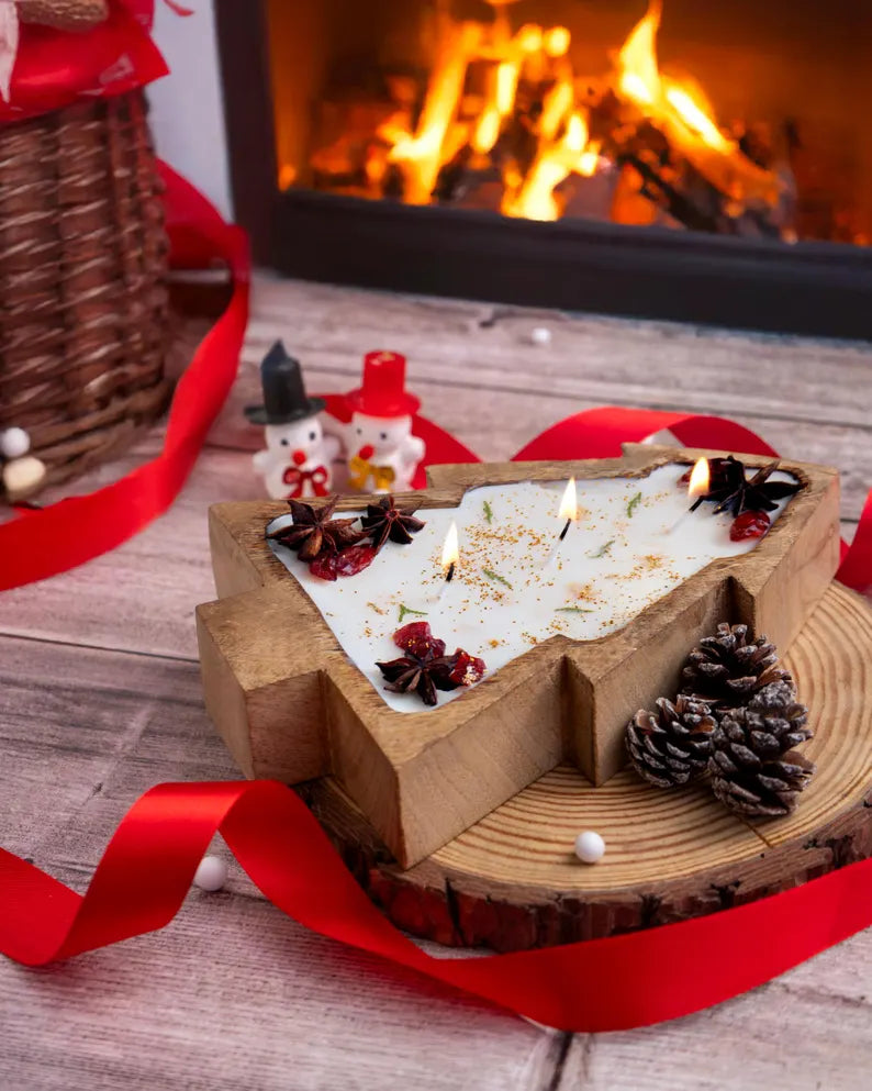 Handmade holiday candle with cranberries and evergreen sprigs in a rustic Christmas tree-shaped bowl by the fireside