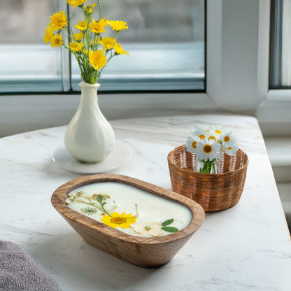 Bowl with candle and flowers on a marble surface with a vase and basket in the background.