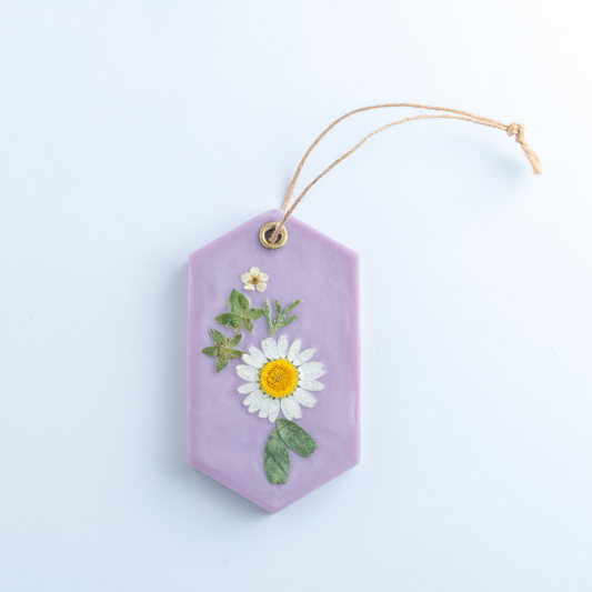 Purple hexagonal hanging ornament with a pressed flower on a light blue background