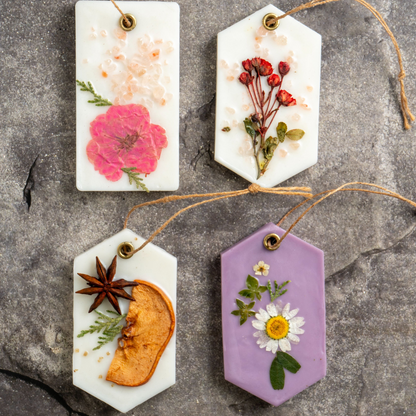 Four decorative tags with pressed flowers and herbs on a textured surface