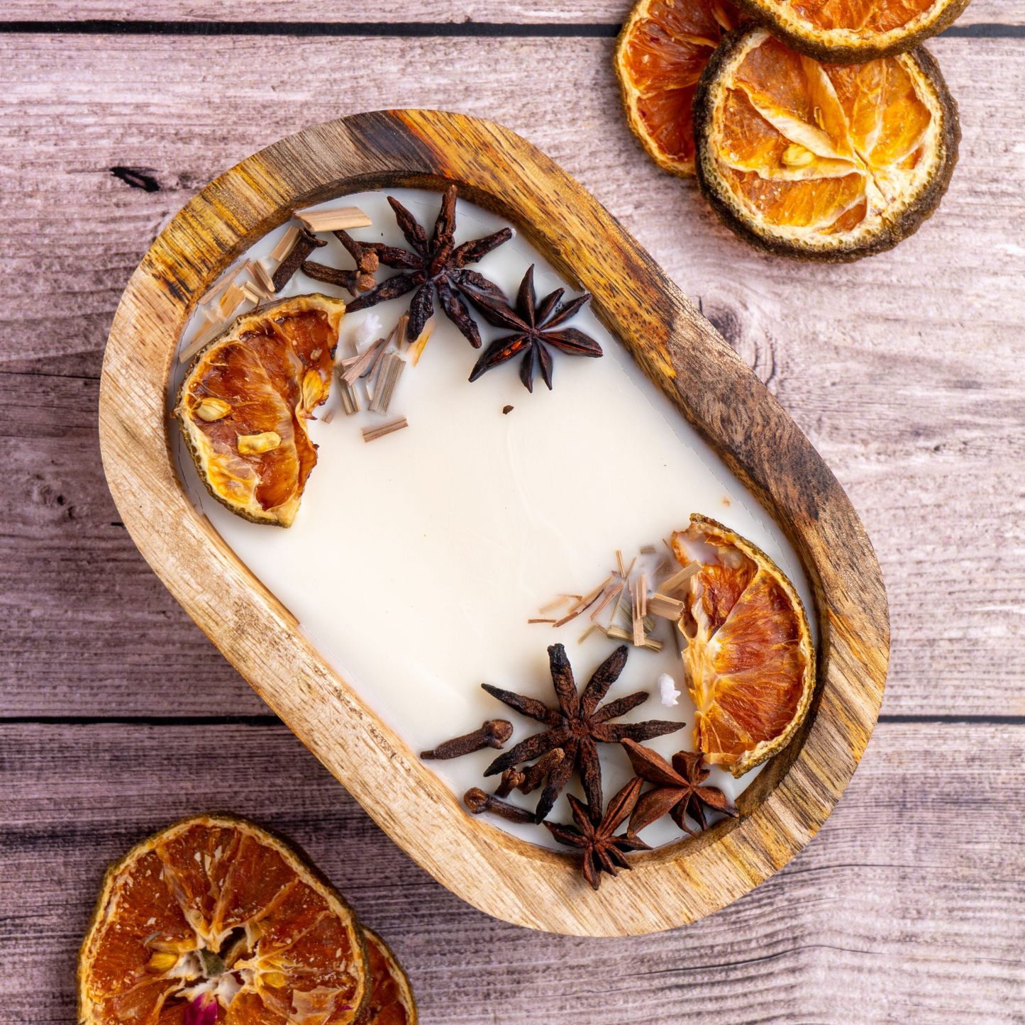 Candle in a wooden holder with dried oranges and star anise on a wooden surface