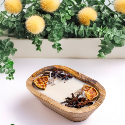 Wooden bowl with a hot chocolate drink garnished with orange slices and star anise, with a plant in the background.