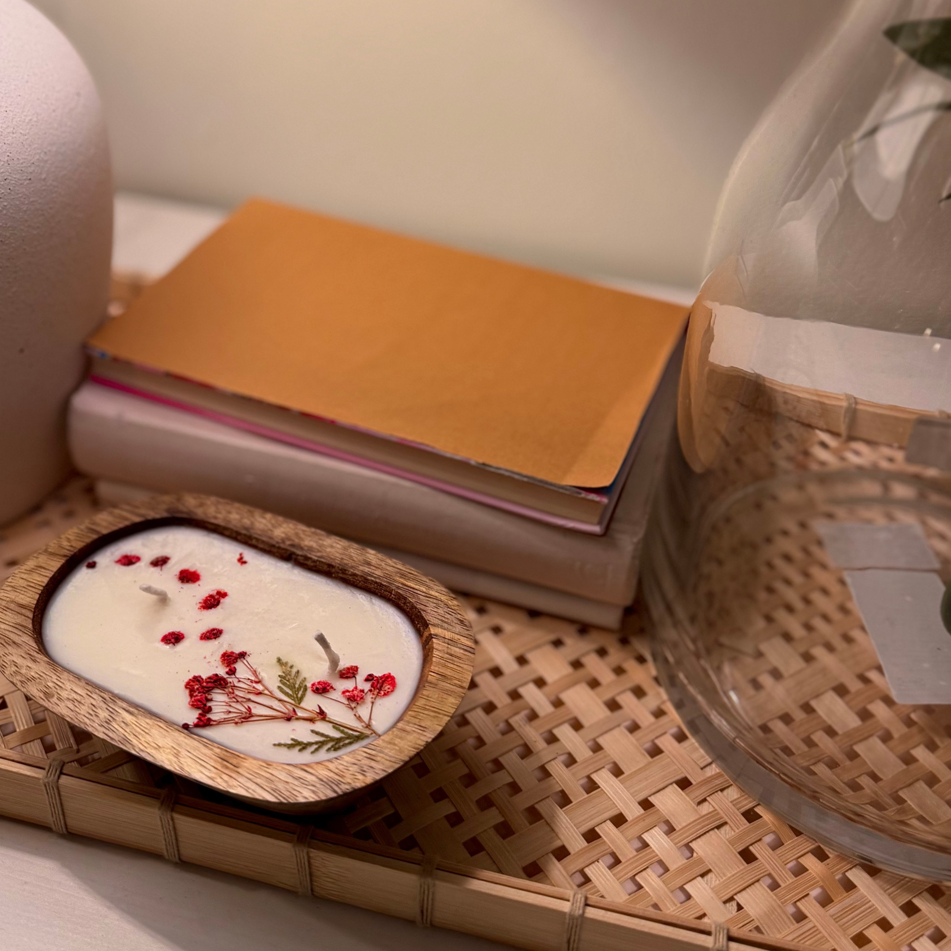 Wooden bowl candle with floral design on a woven mat with books and a glass container.