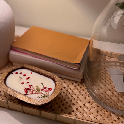 Wooden bowl candle with floral design on a woven mat with books and a glass container.