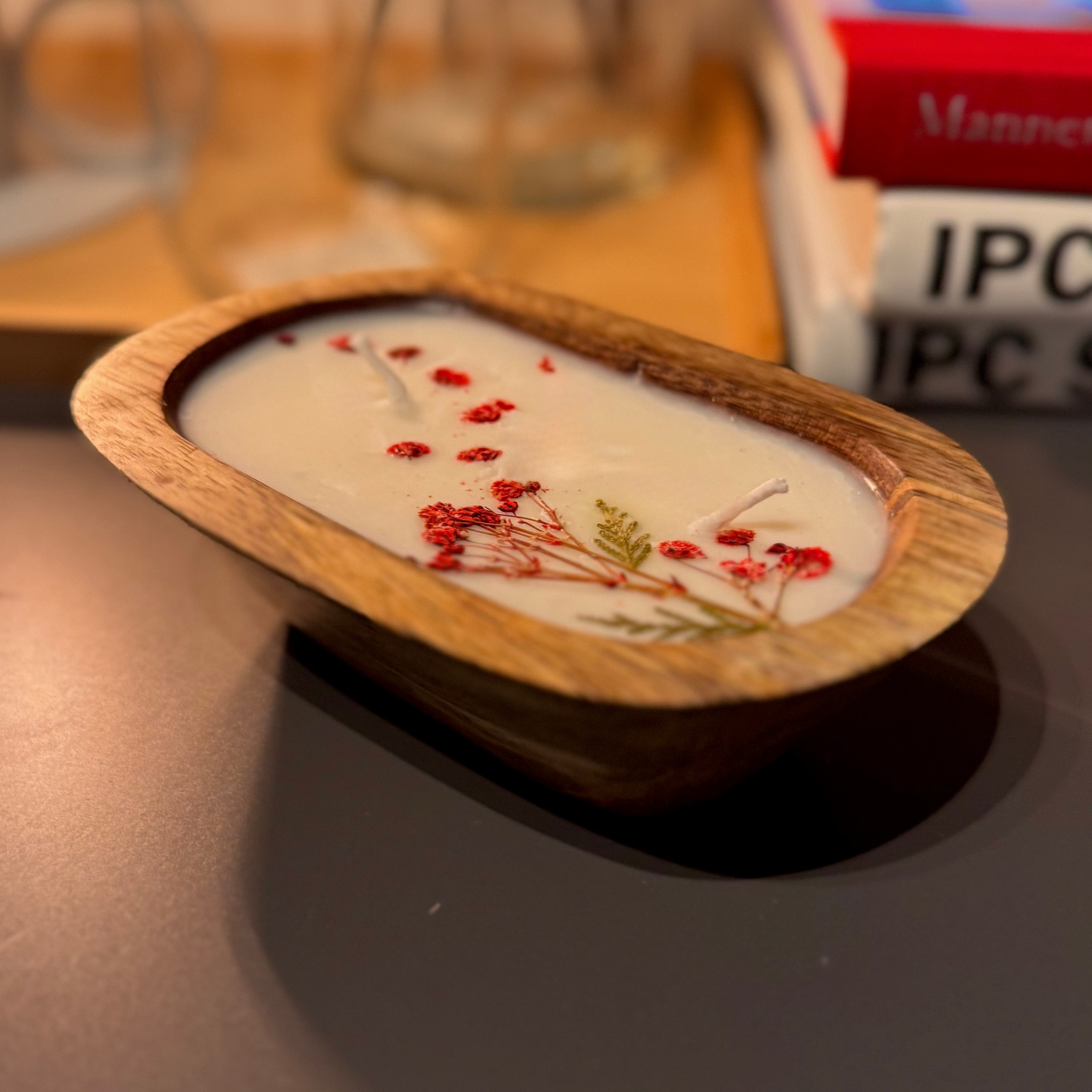 Candle in a wooden holder with floral decorations on a reflective surface.