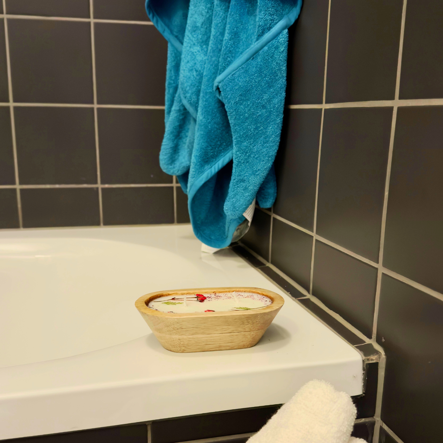 Wooden bowl candle with decorative items on a bathroom counter next to a blue towel.