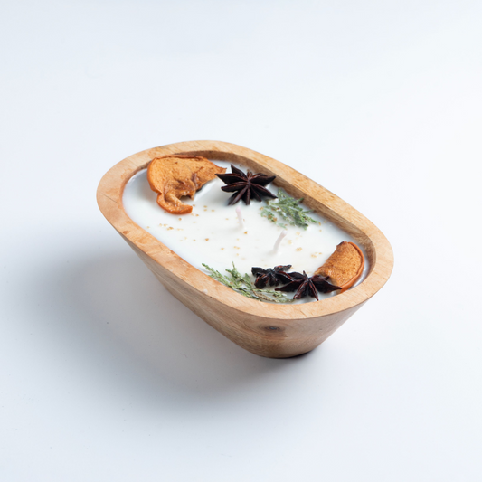 Candle in a wooden dish with star anise and cinnamon on a white background