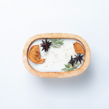 Decorative candle with cinnamon sticks and star anise in a wooden holder on a white background