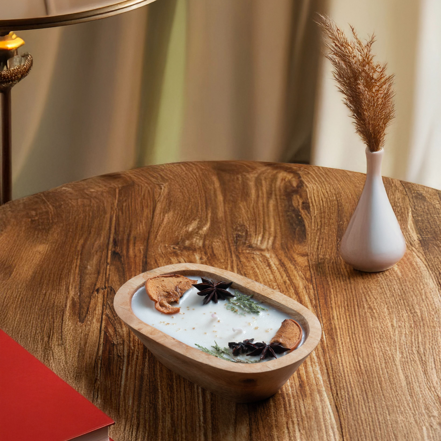 Decorative bowl with dried plants on a wooden table next to a lamp and book
