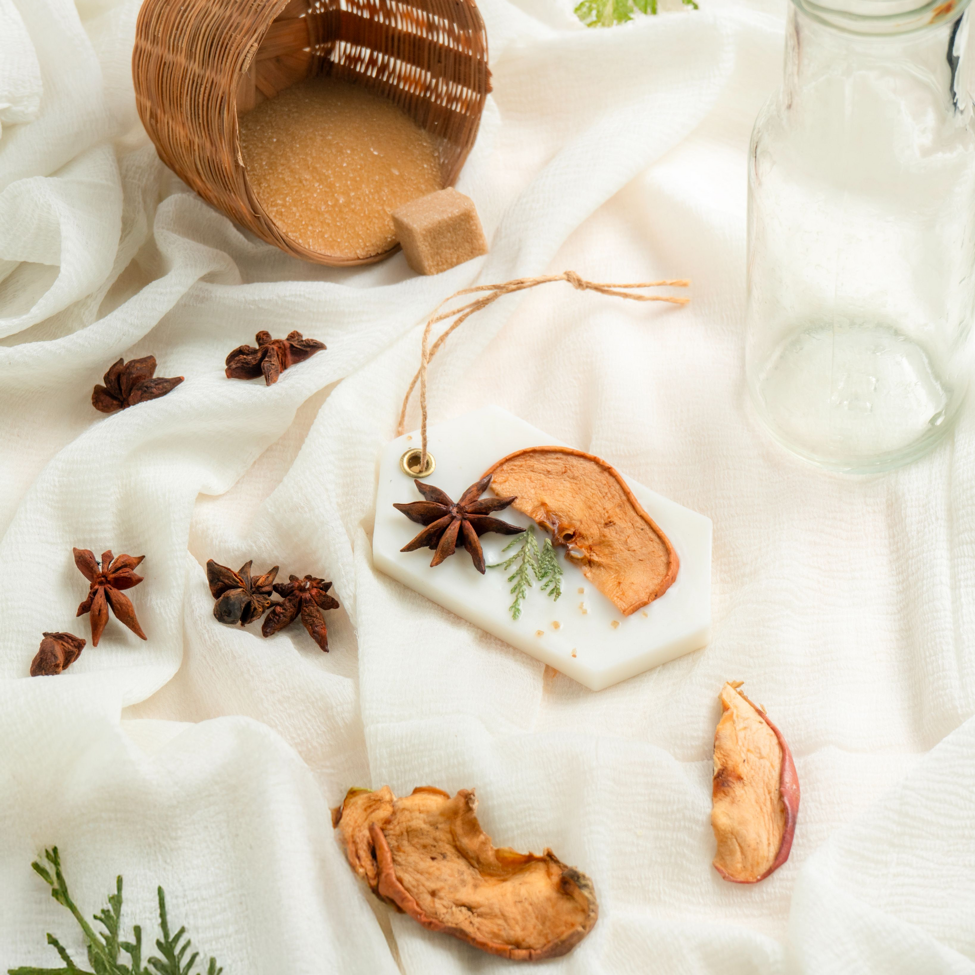 Wooden mug with a beverage, star anise, dried fruit, and a glass bottle on a white fabric background.