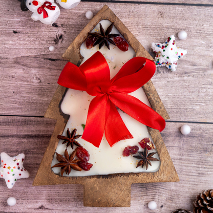Tree-shaped candle with a red bow on a wooden surface with Christmas decorations.