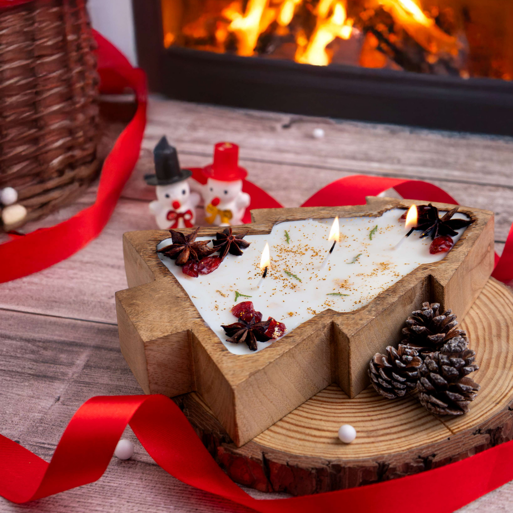 Decorative candle with pine cones and red ribbons in front of a fireplace