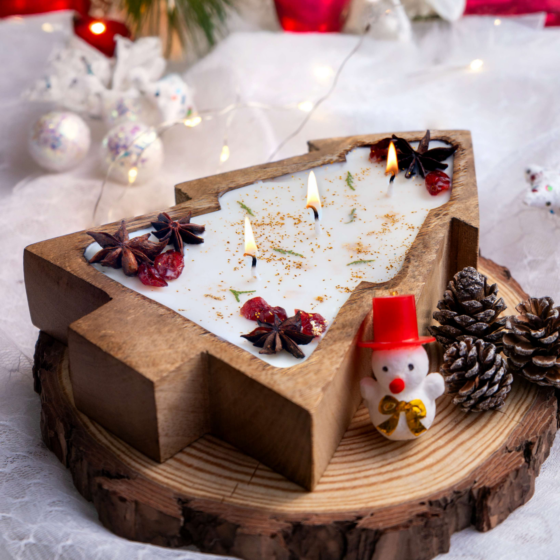 Decorative candle holder with candles, pine cones, and a small snowman figurine on a wooden base.
