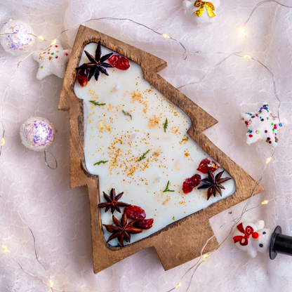 Decorative Christmas tree made of white candle with star anise and cinnamon, surrounded by festive decorations on a light background.