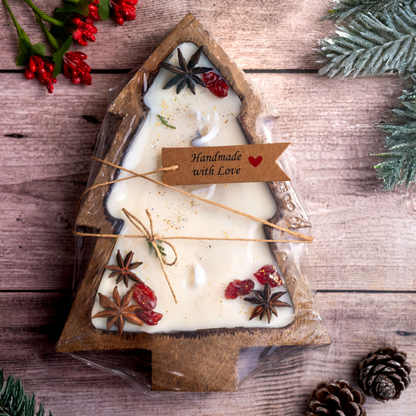Handmade candle in a tree-shaped container with festive decorations on a wooden surface.
