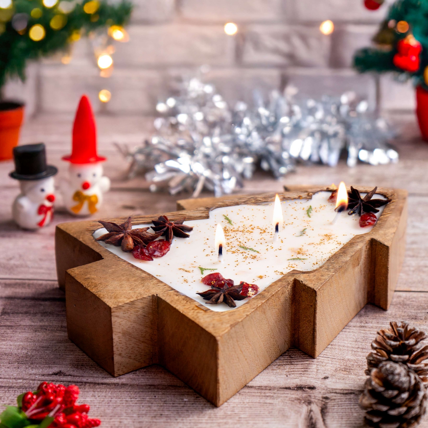 Decorative candle in a wooden holder with Christmas decorations on a wooden surface.