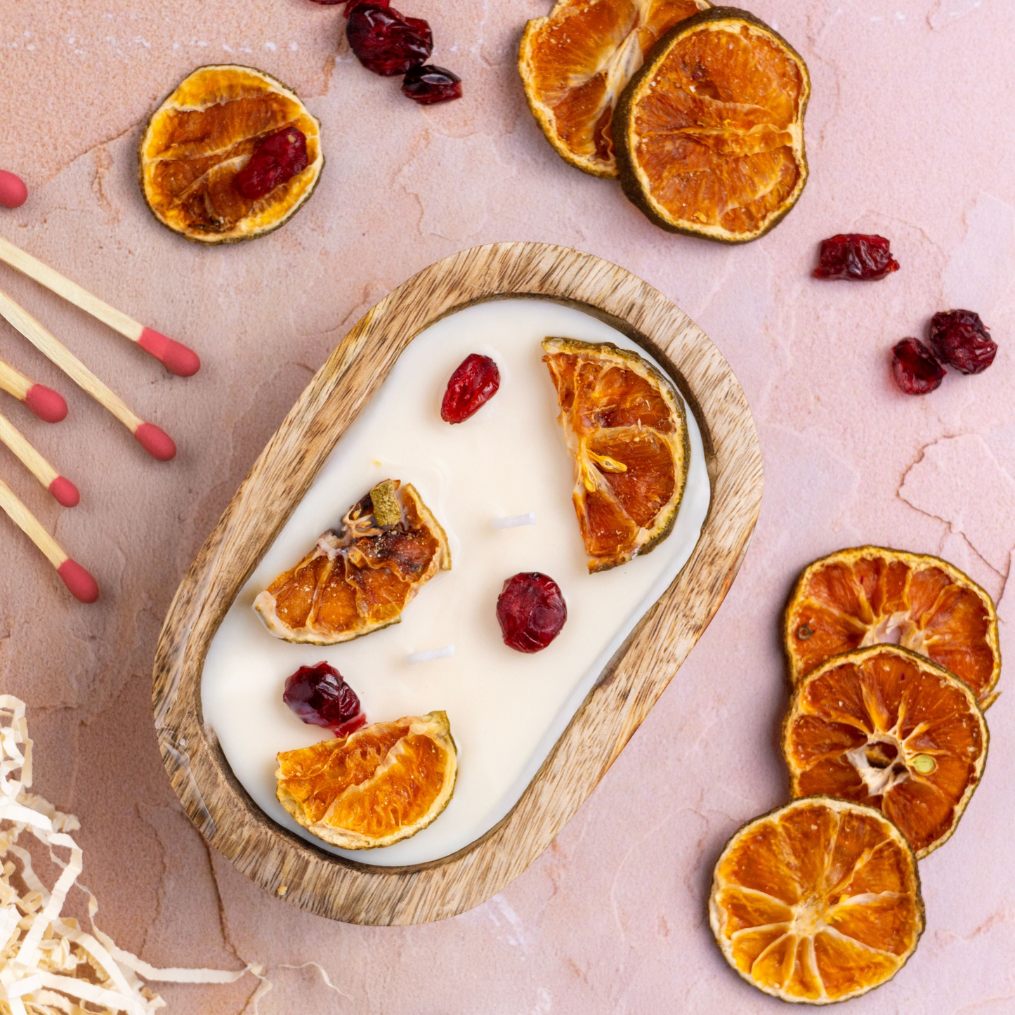 Candle with dried orange slices and cranberries on a wooden tray with matches and decorative elements.