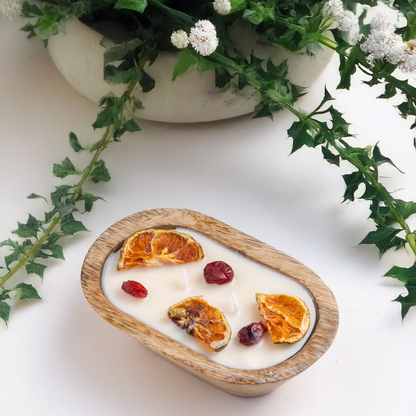 Yogurt with dried fruit and orange slices on a wooden plate, surrounded by greenery.