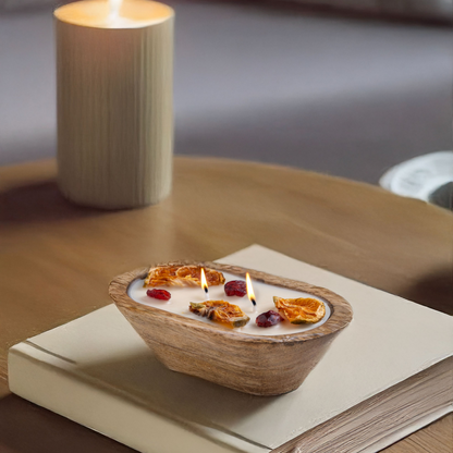 Small wooden bowl with burning candles on a book, next to a lit candle on a wooden surface.