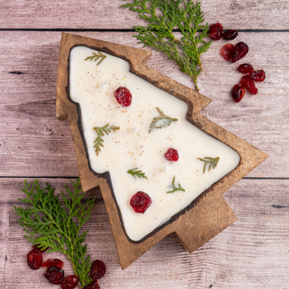 Tree-shaped candle with greenery and berries on a wooden surface