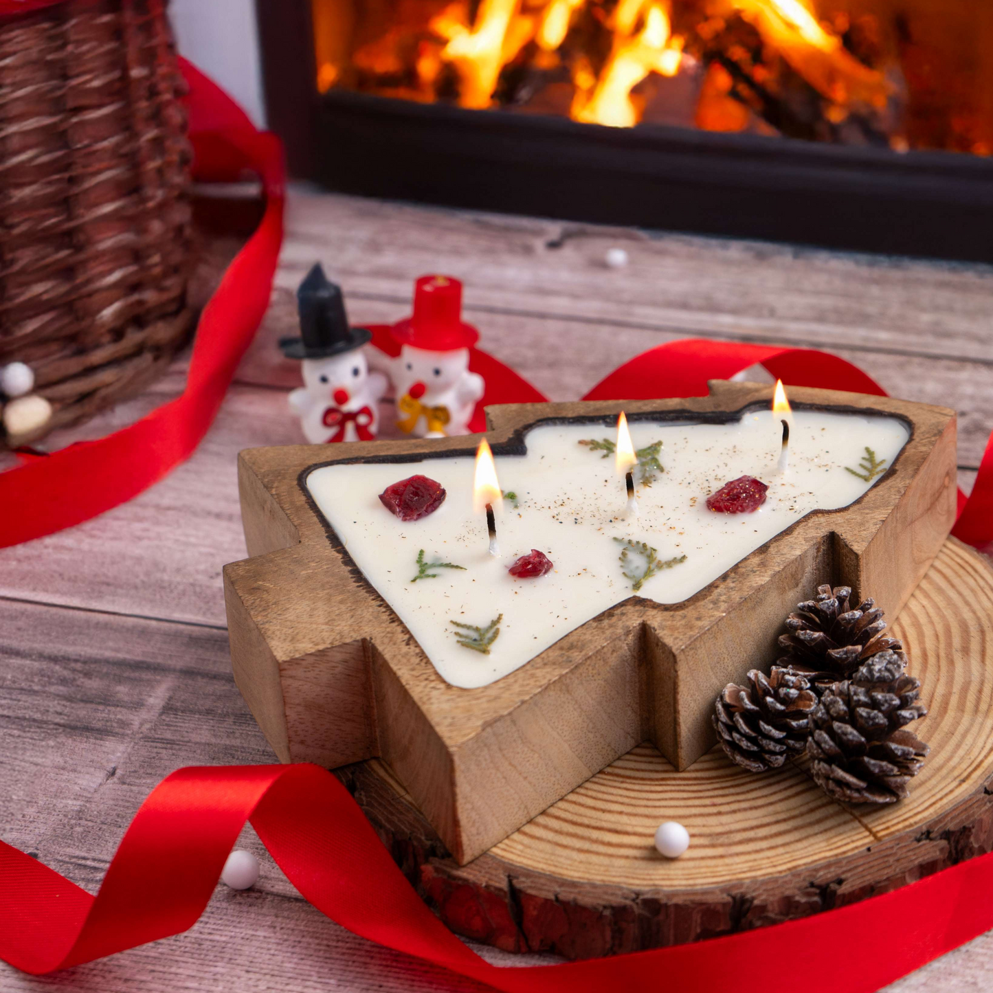 Decorative candle with wooden base and red ribbon in front of a fireplace