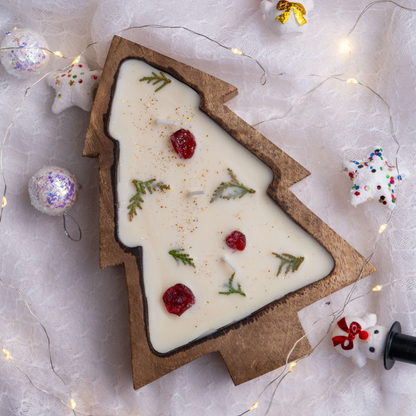 Christmas tree-shaped cookie with white icing, berries, and green leaves on a light gray background with festive decorations.