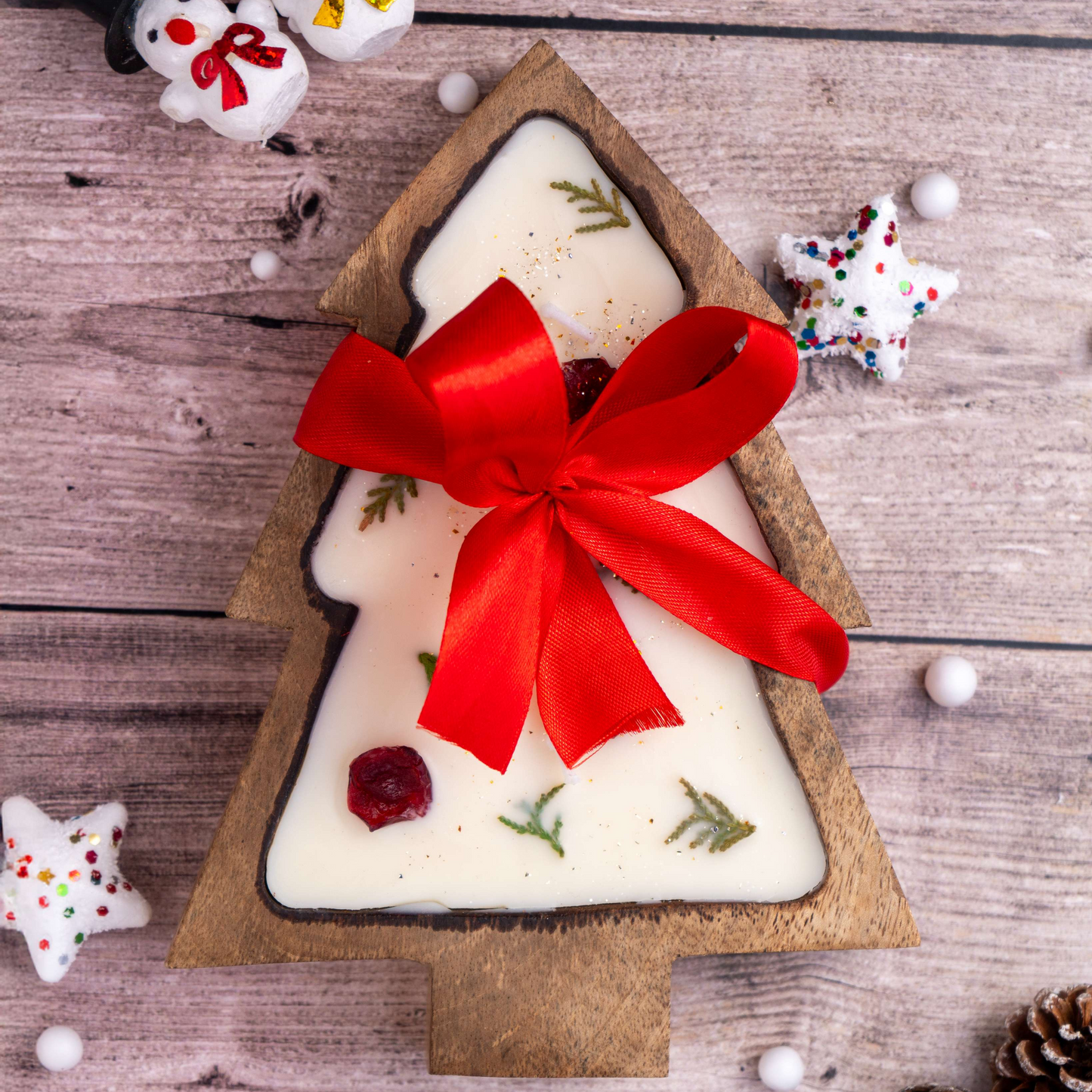 Tree-shaped candle with a red ribbon on a wooden surface with Christmas decorations.