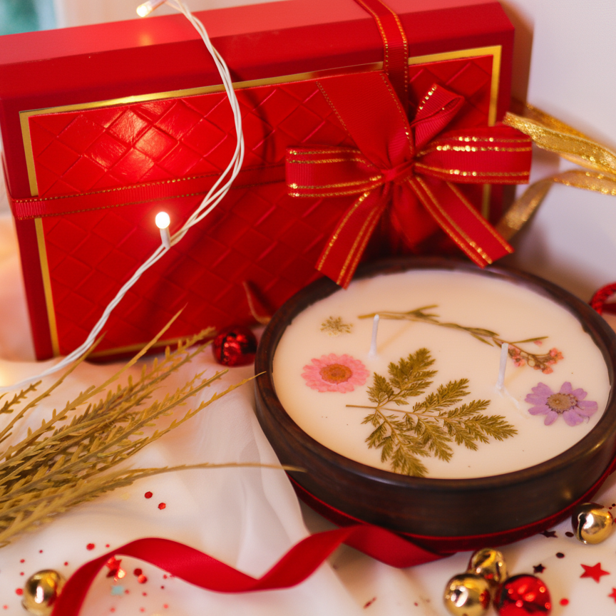 Decorative candle with pressed flowers on a table with a gift box and festive decorations.