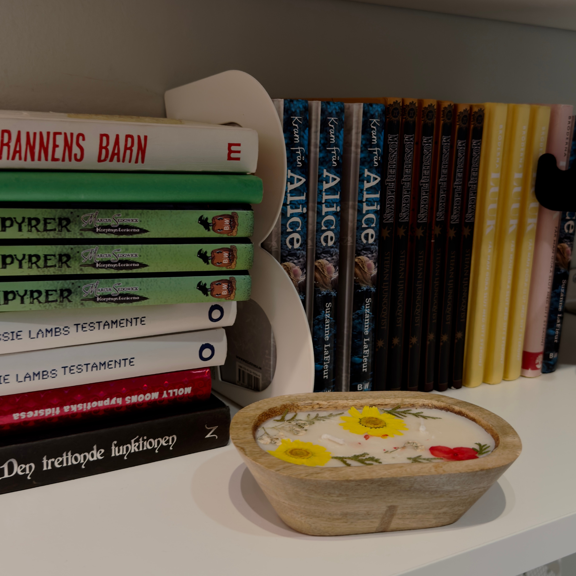 Stack of books with a decorative wooden box candle featuring floral designs on a shelf.