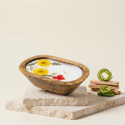 Wooden bowl candle featuring flowers on a stone platform.