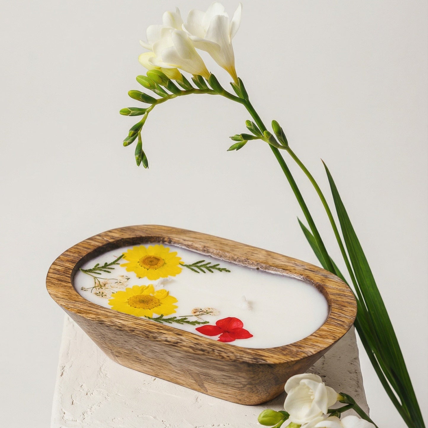 Decorative candle with floral design on a white pedestal with flowers in the background