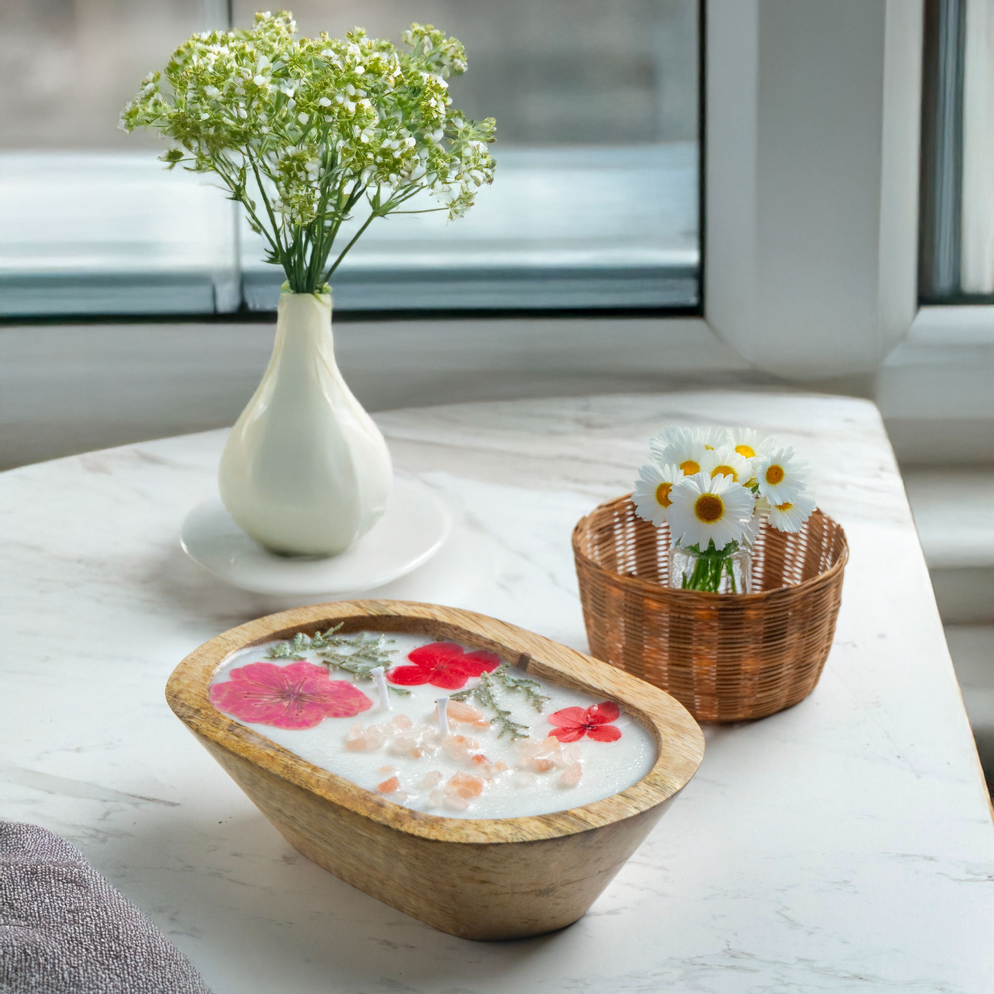 Decorative items including a white vase with flowers, a wicker basket with flowers, and a woven bowl with floral design on a light surface.