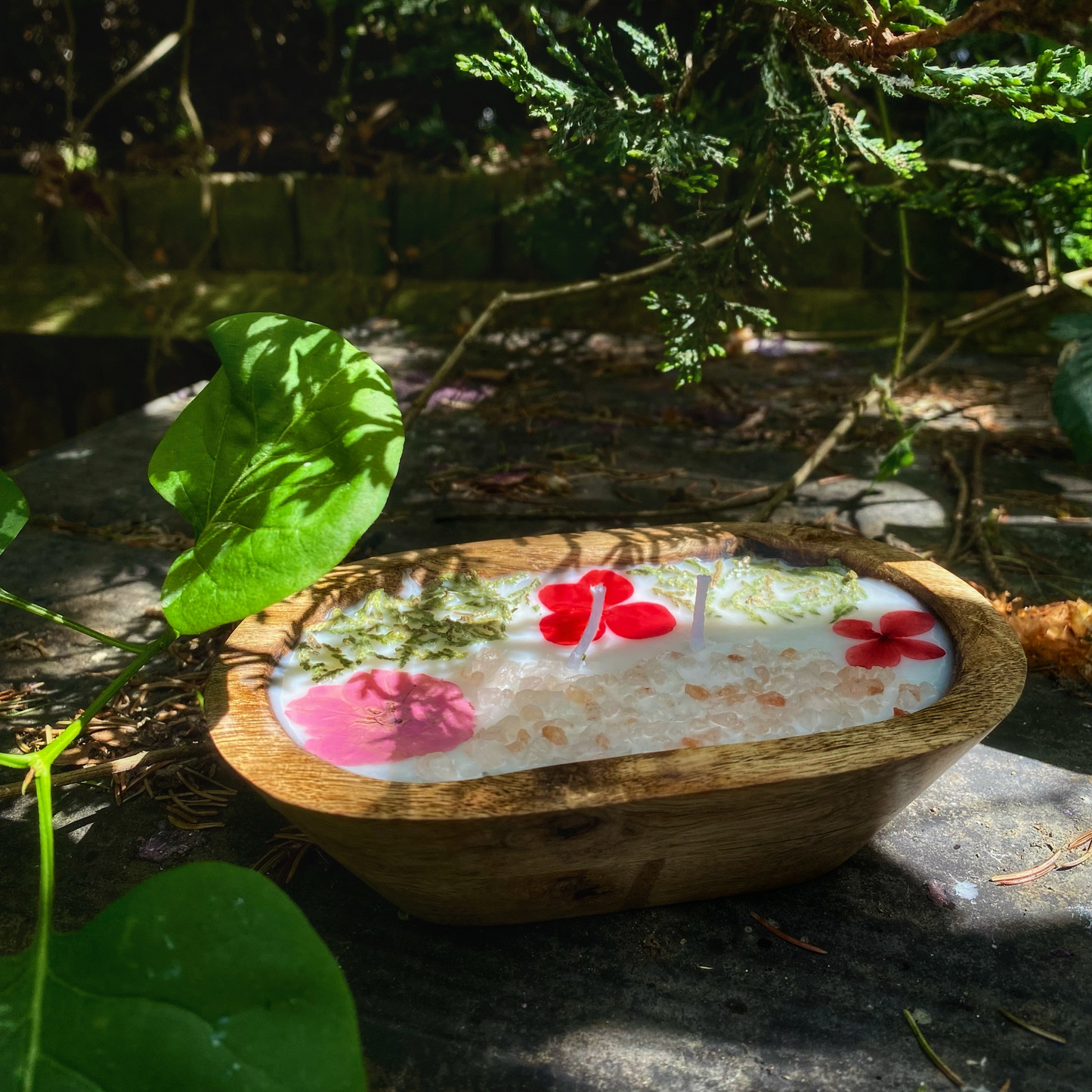 Wooden bowl with floral design on a stone surface with greenery in the background