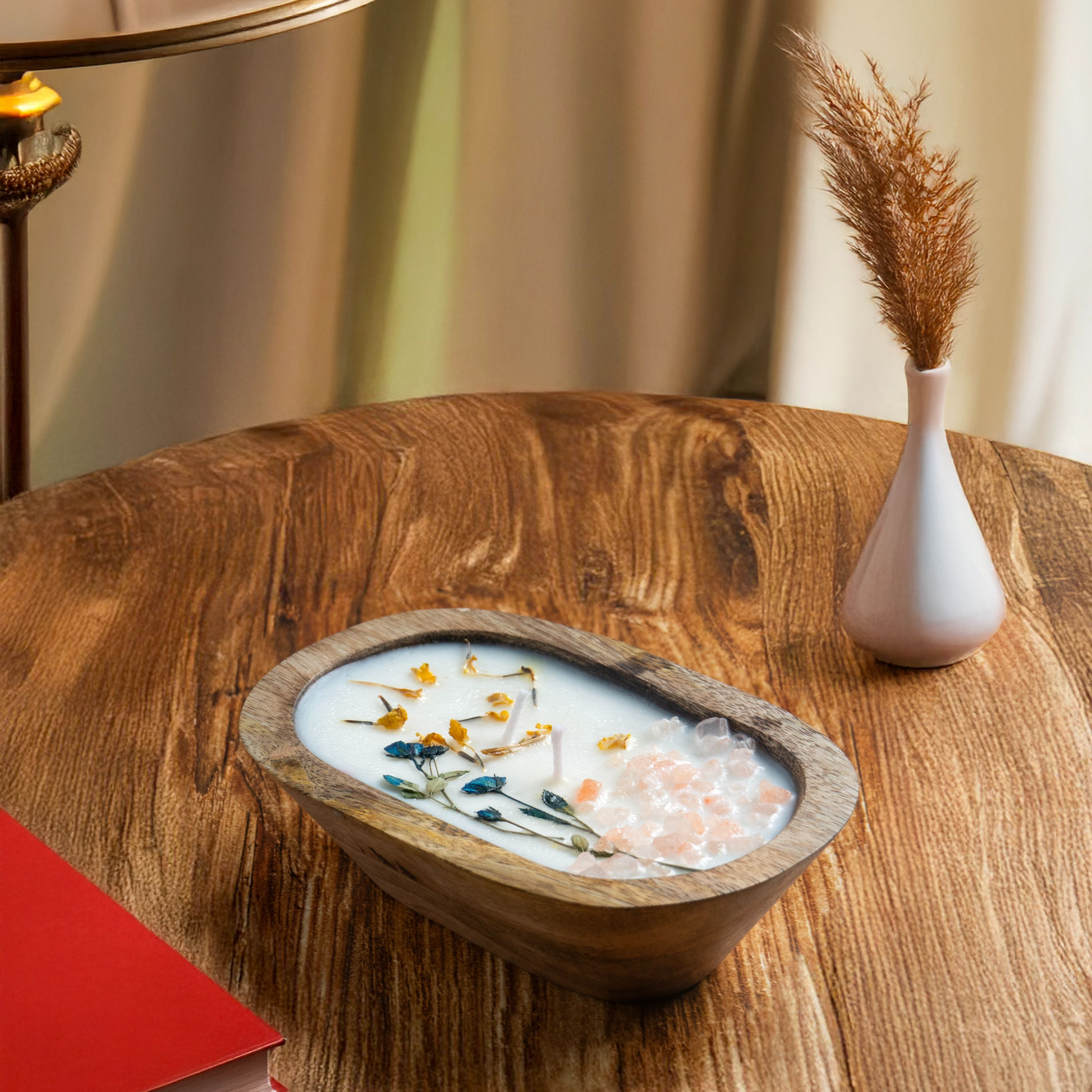 Decorative bowl with flowers on a wooden table next to a lamp and vase.
