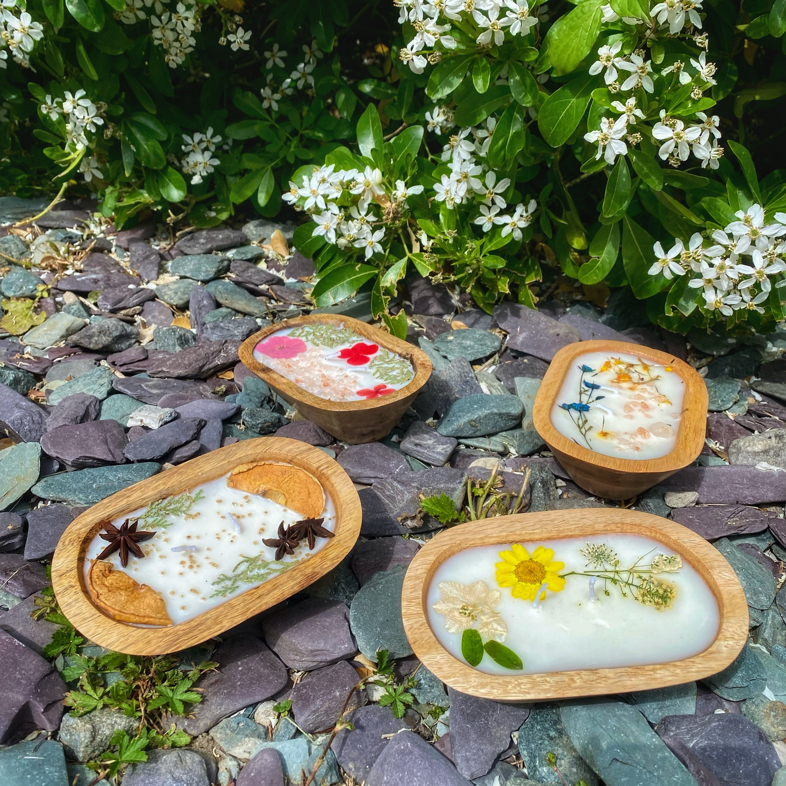 Four small wooden bowls with decorative elements on a stone surface with flowers in the background
