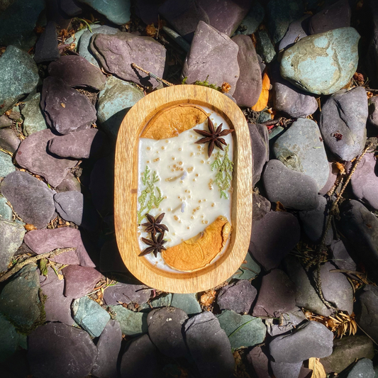 Wooden dish with a white substance, star anise, and orange pieces on a bed of multicolored stones.